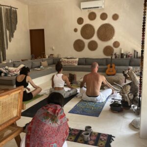 A woman playing an acoustic guitar during a sound healing meditation session in a limestone cave with candles and crystal bowls.