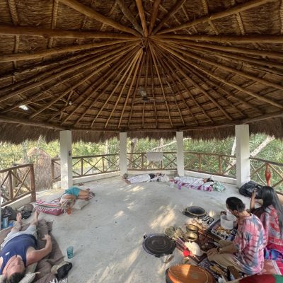 A woman playing an acoustic guitar during a sound healing session in a limestone cave with candles and crystal singing bowls.