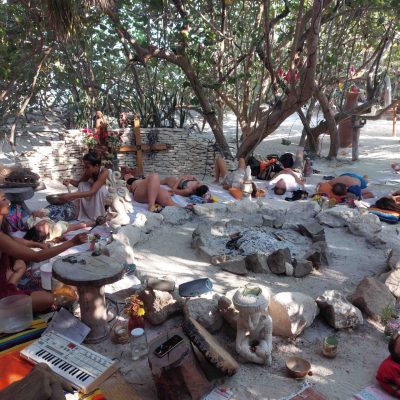 A woman playing an acoustic guitar and crystal singing bowls during a sound healing meditation session inside a limestone cave.